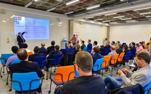 Homem de terno apresenta PowerPoint para grupo de profissionais em ampla sala de aula