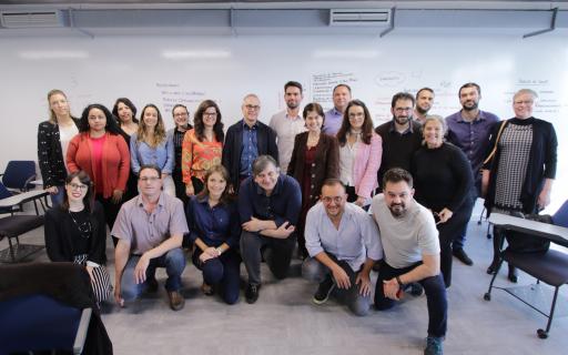 Grupo de 22 pessoas posa para foto com quadro branco ao fundo.